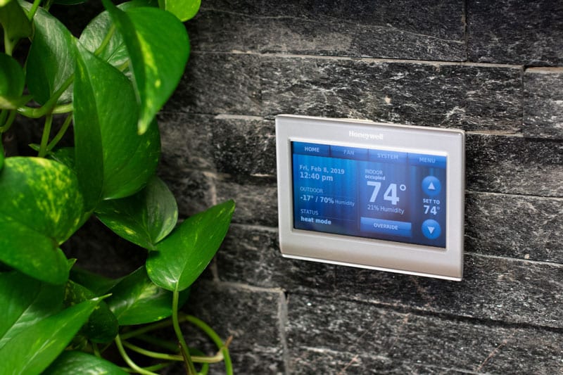 A programmable thermostat on a gray brick wall