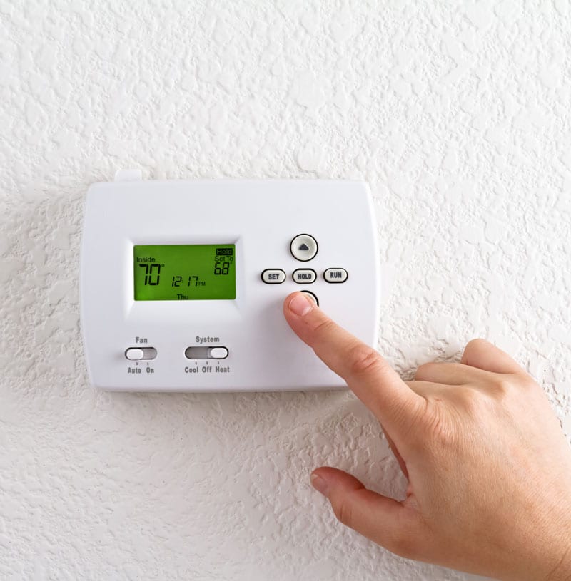 A close-up of a person’s hand adjusting a thermostat on a white wall