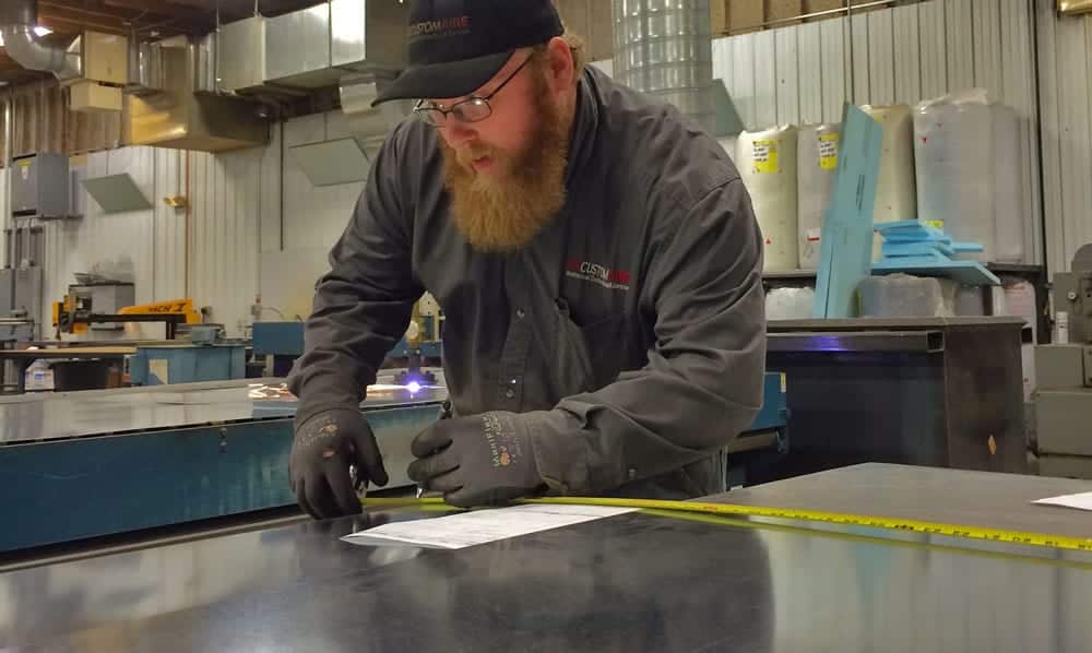 A Custom Aire technician measures a piece of sheet metal in a fabrication shop