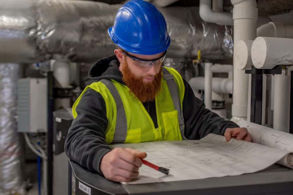 A male HVAC technician looking down at a blueprint of sheet metal ductwork