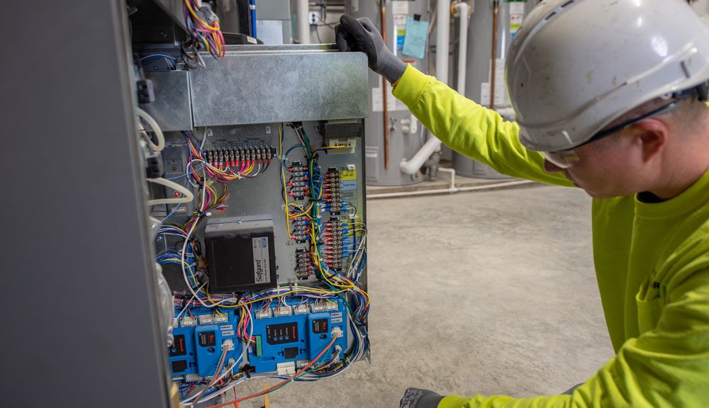 A male HVAC technician inspects the inner wires of a commercial boiler