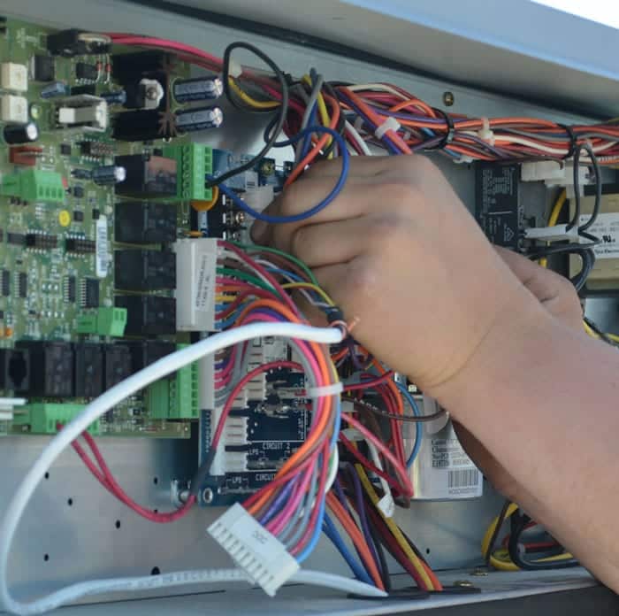 A closeup of a technician’s hands adjusting internal wires of a commercial HVAC system