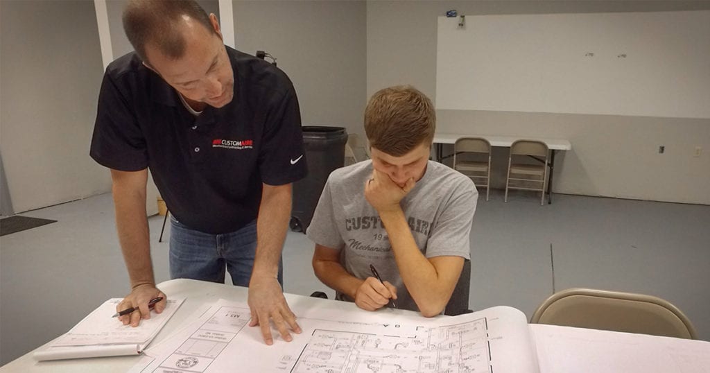 A male instructor and a student reviewing an HVAC construction plan together during Custom Aire’s apprenticeship program