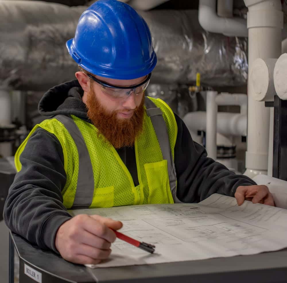 A male HVAC technician looking down at a blueprint of a commercial HVAC system