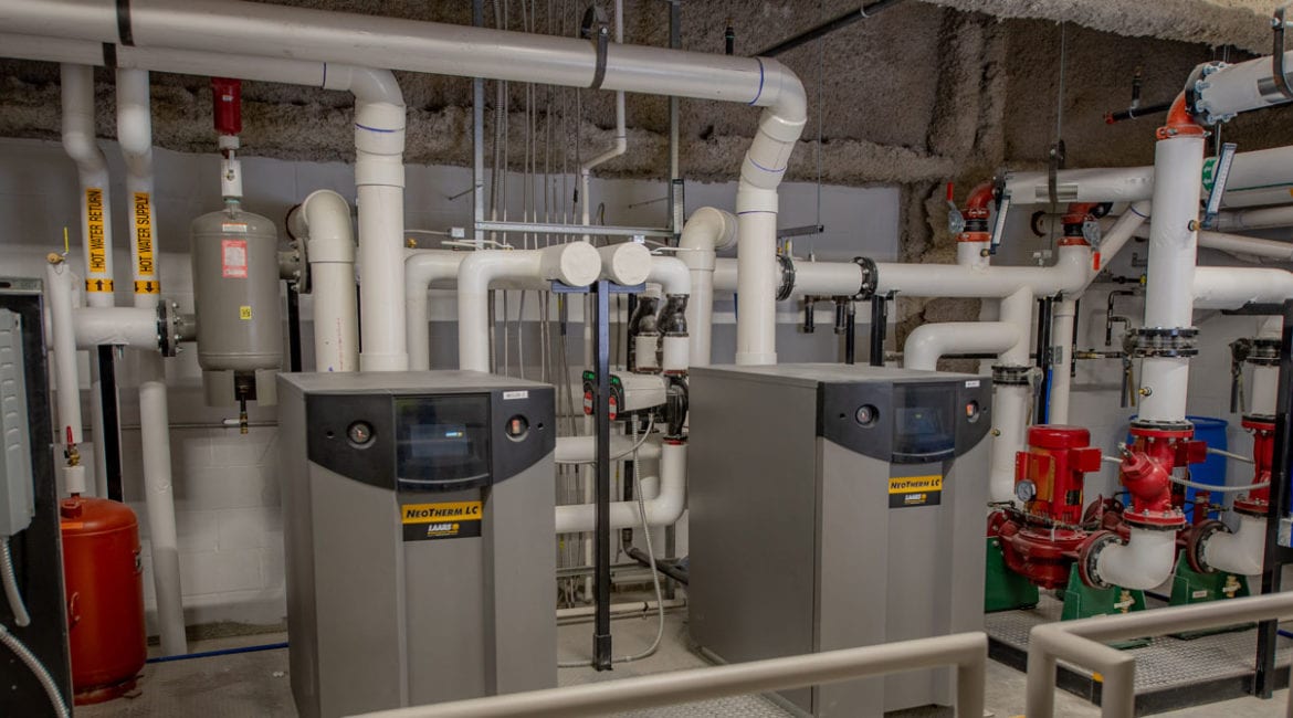 Two LAARS commercial boilers sitting next to one another in the mechanical room of an apartment building