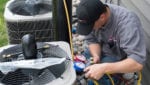 A male Custom Aire HVAC service technician checks the pressure on a set of commercial air conditioners outside an apartment complex