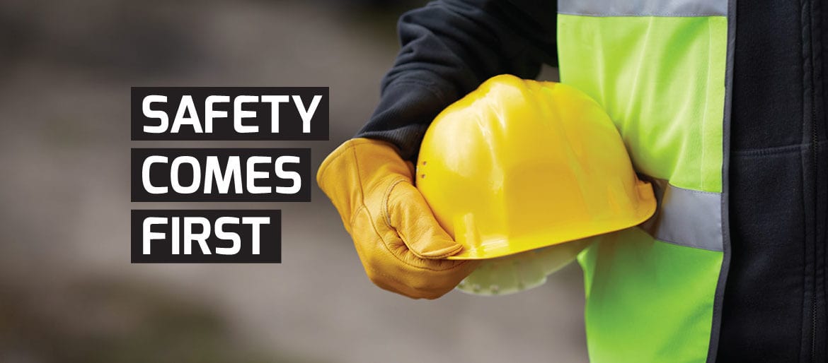 A closeup of a construction worker holding a yellow hardhat while wearing gloves and a safety vest