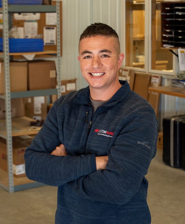 Youthful HVAC technician in the warehouse, smiling confidently at the camera